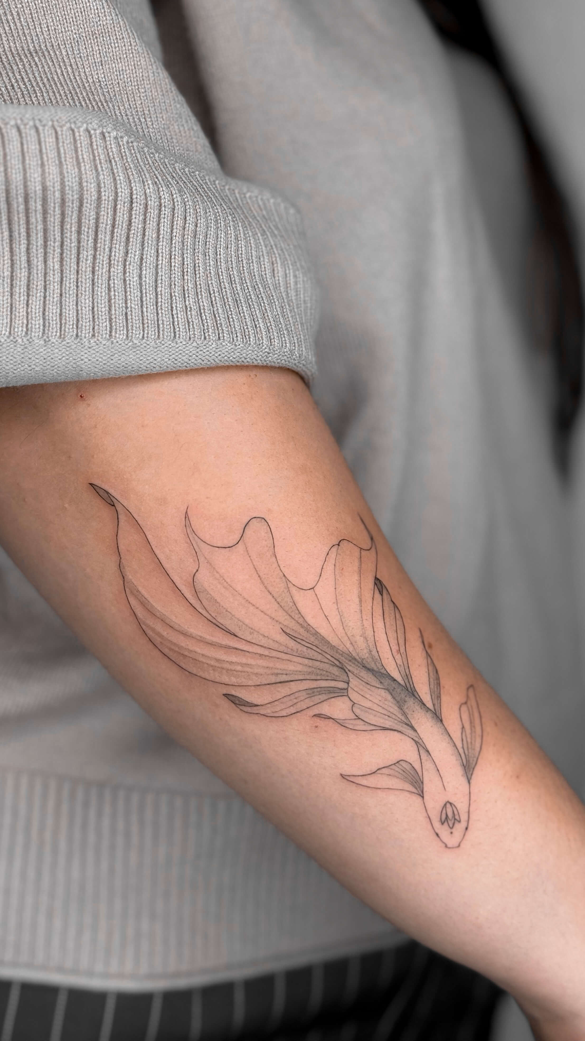 Fine line fish tattoo on the arm